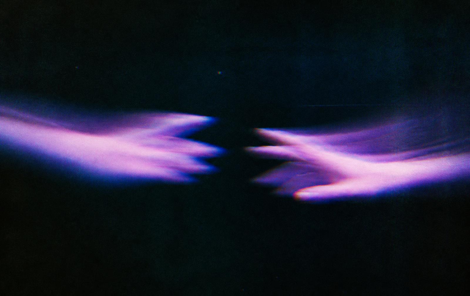 Two blurred hands reaching toward each other in low light